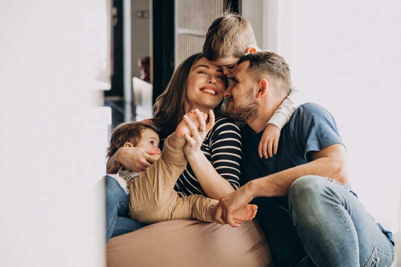 Fotografía de una familia feliz con dos niños, sonriente y tranquila en el sofá de su casa.