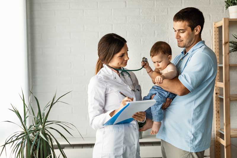 Fotografía de un padre llevando a su hijo pequeño a la pediatra.