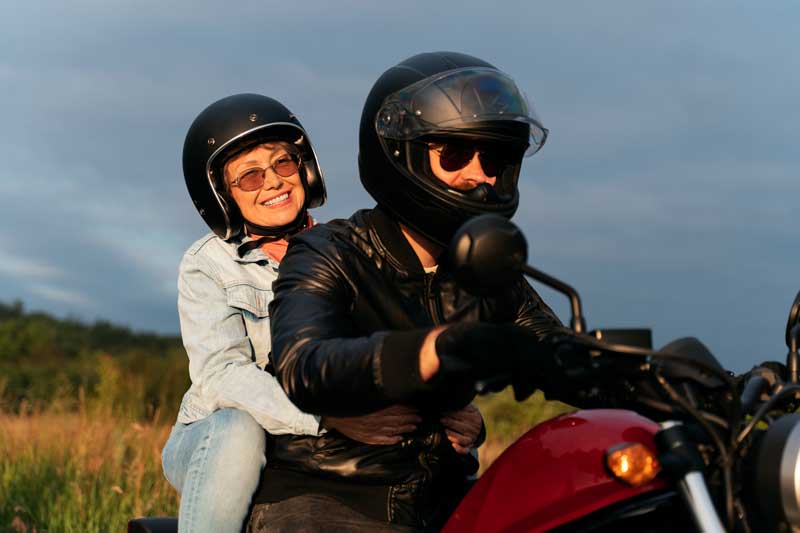Fotografía de una pareja de edad, subida en una moto con sus cascos.